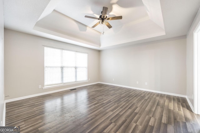 spare room featuring ceiling fan, dark wood-type flooring, and a raised ceiling