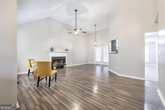 living room with ceiling fan with notable chandelier, dark wood-type flooring, and high vaulted ceiling