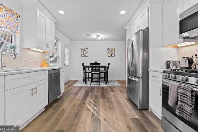 kitchen featuring appliances with stainless steel finishes, backsplash, dark wood-type flooring, white cabinets, and sink