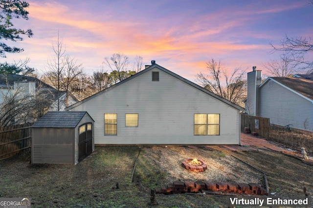 back house at dusk with a fire pit and a storage unit