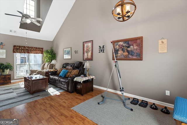 living room featuring a towering ceiling, wood-type flooring, and ceiling fan with notable chandelier