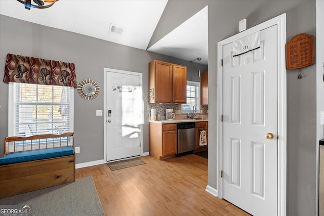 kitchen with sink, vaulted ceiling, dishwasher, light hardwood / wood-style floors, and decorative backsplash