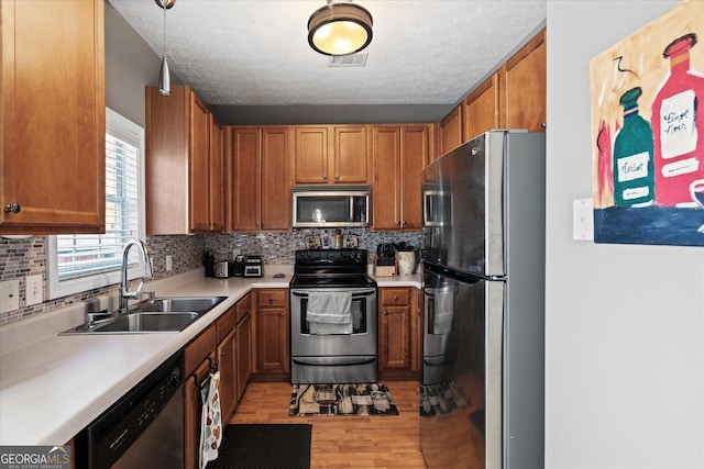 kitchen with a textured ceiling, pendant lighting, light hardwood / wood-style floors, appliances with stainless steel finishes, and sink