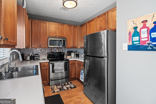 kitchen with a textured ceiling, stainless steel appliances, light hardwood / wood-style floors, backsplash, and sink