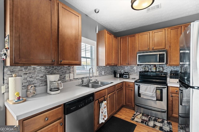 kitchen featuring light hardwood / wood-style flooring, pendant lighting, backsplash, appliances with stainless steel finishes, and sink