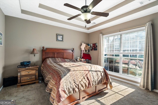 carpeted bedroom with a raised ceiling and ceiling fan