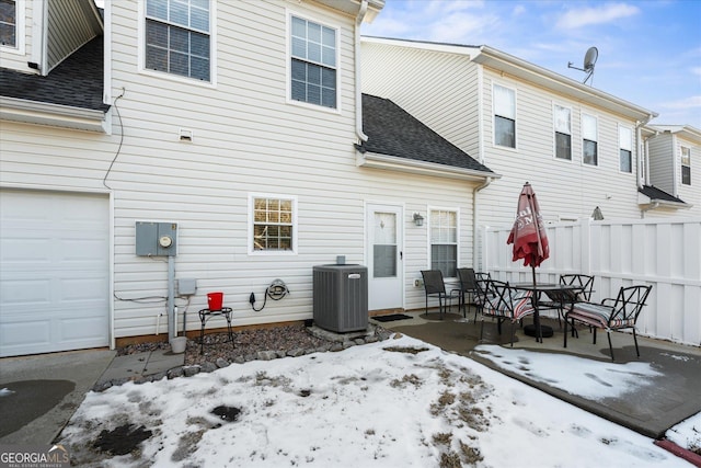 snow covered rear of property featuring a patio, central AC, and a garage