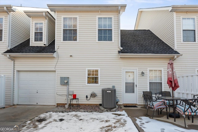 snow covered rear of property featuring a garage and central AC unit