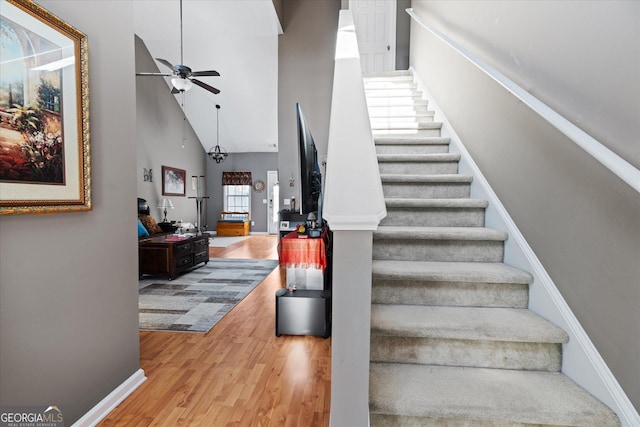 stairway featuring ceiling fan, a towering ceiling, and wood-type flooring