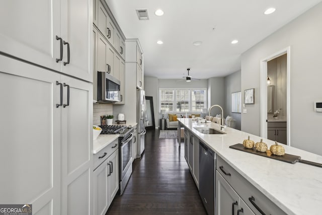 kitchen featuring stainless steel appliances, sink, ceiling fan, backsplash, and light stone countertops