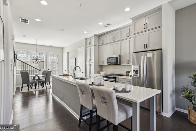 kitchen with sink, a breakfast bar area, gray cabinetry, hanging light fixtures, and appliances with stainless steel finishes