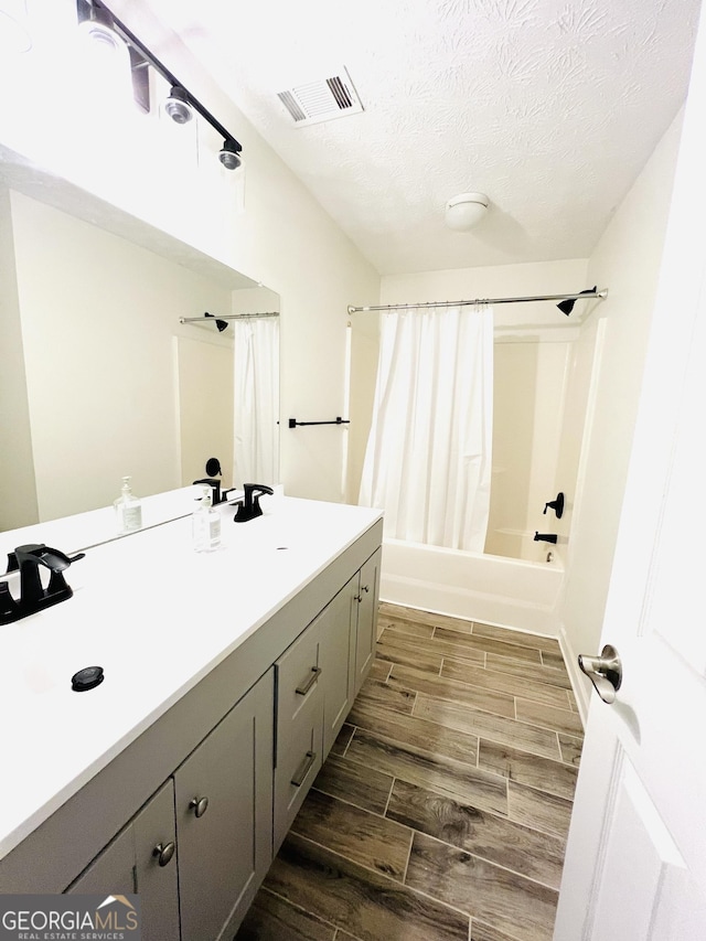 bathroom with a textured ceiling, shower / bath combination with curtain, and vanity