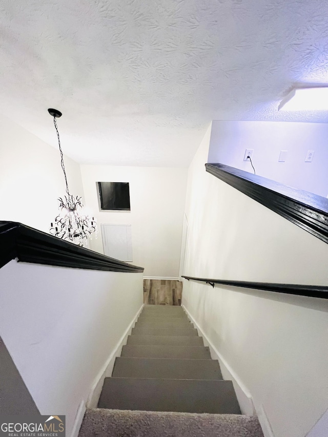 stairway with a textured ceiling and a notable chandelier