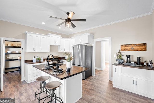 kitchen with sink, white cabinets, a breakfast bar area, stainless steel refrigerator, and a kitchen island with sink