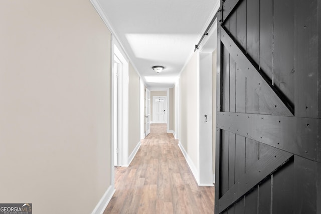 hallway with ornamental molding, a barn door, and light hardwood / wood-style floors