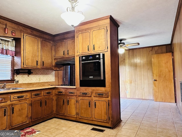 kitchen featuring ceiling fan, wood walls, sink, stainless steel oven, and light tile patterned floors