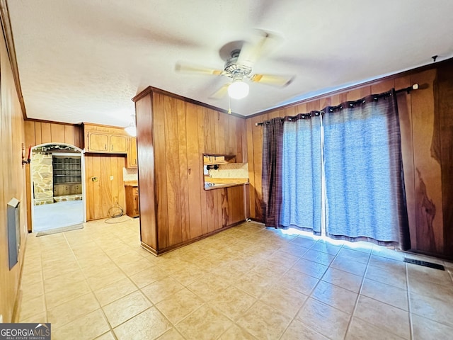 kitchen featuring ceiling fan, light tile patterned flooring, ornamental molding, and wooden walls