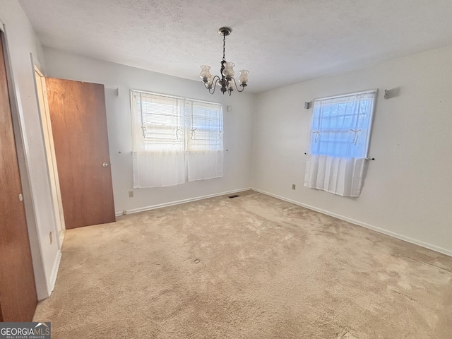 carpeted empty room with a textured ceiling and a chandelier