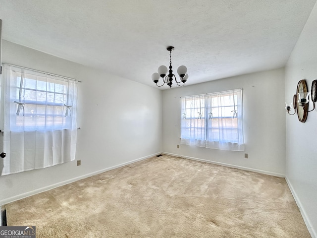 spare room with a textured ceiling, light colored carpet, plenty of natural light, and a notable chandelier