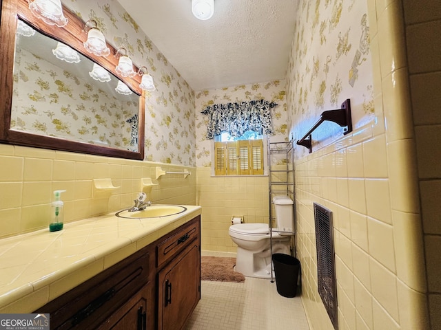 bathroom with toilet, vanity, tile walls, tile patterned flooring, and a textured ceiling