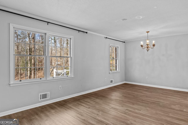 empty room featuring hardwood / wood-style flooring, an inviting chandelier, ornamental molding, and a textured ceiling