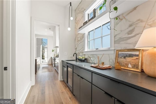 bar featuring decorative light fixtures, light hardwood / wood-style flooring, a wealth of natural light, and sink