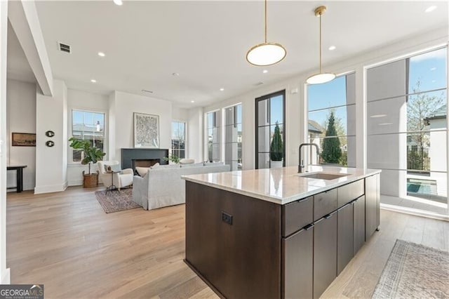 kitchen with pendant lighting, sink, an island with sink, light wood-type flooring, and dark brown cabinetry