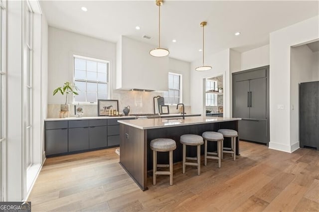 kitchen with paneled built in refrigerator, an island with sink, pendant lighting, light hardwood / wood-style flooring, and white cabinetry