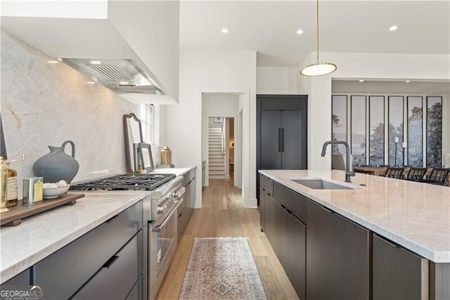 kitchen featuring light stone countertops, wall chimney exhaust hood, pendant lighting, high end stove, and sink