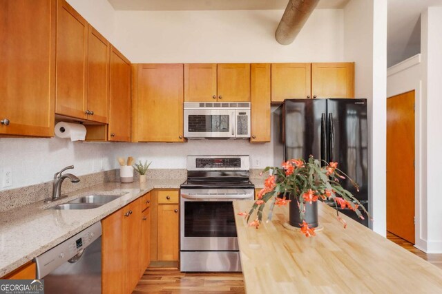 kitchen featuring stainless steel appliances, sink, light hardwood / wood-style floors, and light stone countertops