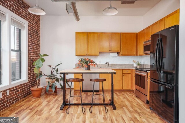 kitchen with brick wall, light hardwood / wood-style floors, pendant lighting, and appliances with stainless steel finishes