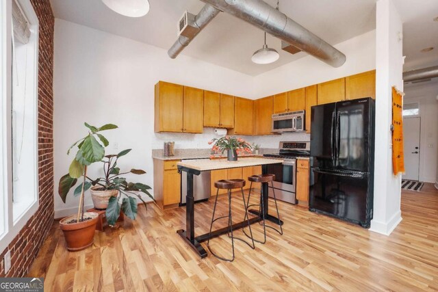 kitchen with stainless steel appliances, a towering ceiling, a kitchen breakfast bar, and light hardwood / wood-style floors