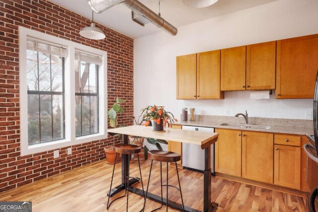 kitchen with sink, light wood-type flooring, stainless steel dishwasher, light stone countertops, and brick wall