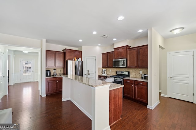 kitchen with decorative backsplash, light stone countertops, appliances with stainless steel finishes, and a center island with sink