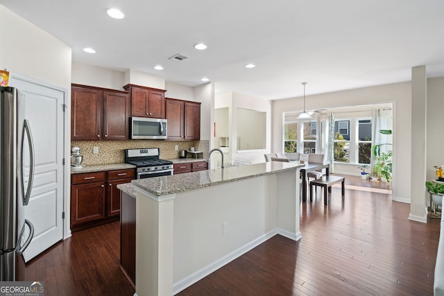 kitchen with decorative light fixtures, an island with sink, light stone countertops, and appliances with stainless steel finishes