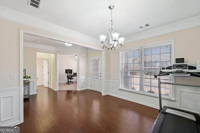 exercise area with ceiling fan with notable chandelier, dark wood-type flooring, and ornamental molding