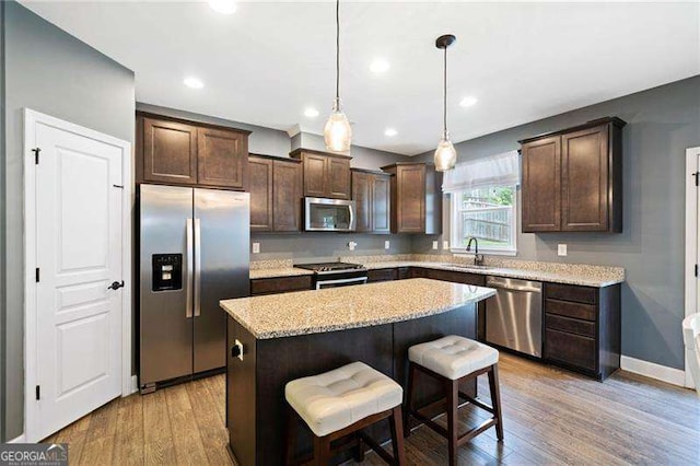 kitchen featuring hanging light fixtures, a kitchen island, a breakfast bar area, appliances with stainless steel finishes, and sink