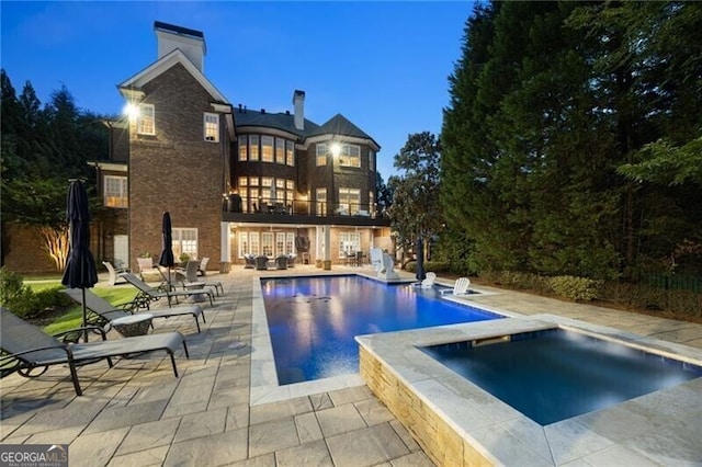 pool at dusk with an in ground hot tub and a patio area