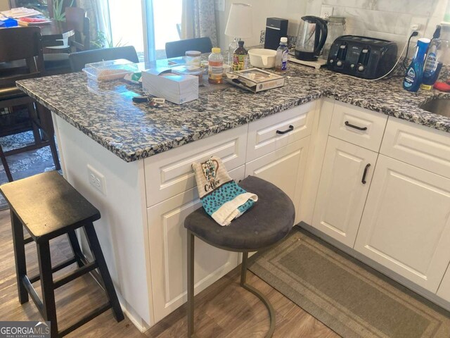 kitchen featuring dark stone counters, white cabinetry, a kitchen bar, and wood-type flooring