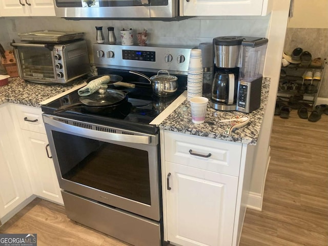 kitchen featuring white cabinets, light hardwood / wood-style floors, dark stone counters, and stainless steel electric stove