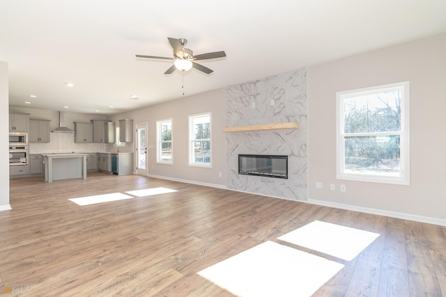 unfurnished living room featuring a premium fireplace, ceiling fan, and light hardwood / wood-style flooring