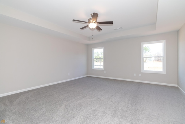 carpeted empty room with ceiling fan and a raised ceiling