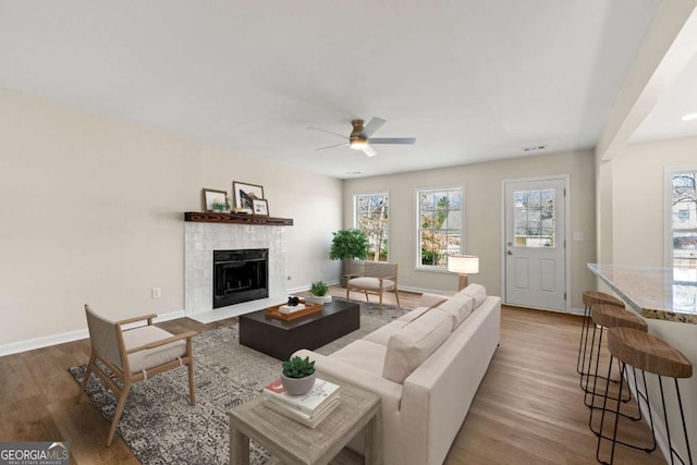 living room featuring wood-type flooring, a tiled fireplace, and ceiling fan