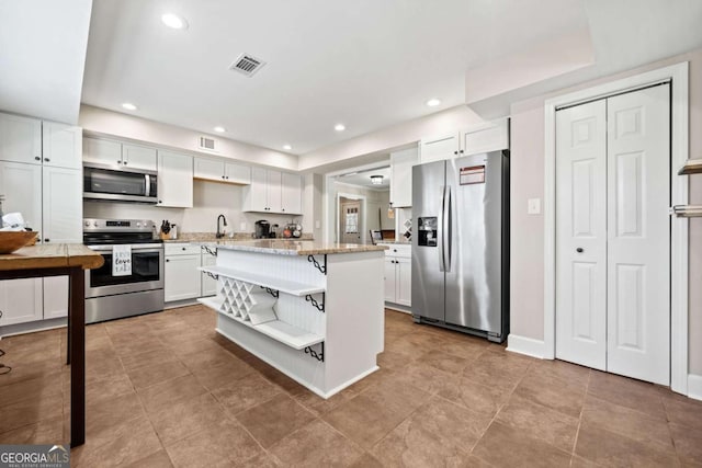 kitchen featuring light stone counters, a center island, a kitchen bar, white cabinets, and appliances with stainless steel finishes