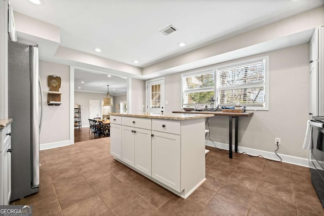 kitchen featuring stainless steel refrigerator, light stone countertops, a kitchen island, white cabinets, and decorative light fixtures