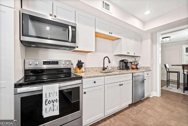 kitchen featuring light stone counters, white cabinets, appliances with stainless steel finishes, and sink