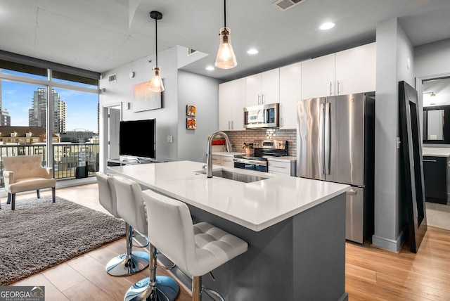 kitchen with stainless steel appliances, pendant lighting, expansive windows, decorative backsplash, and white cabinets