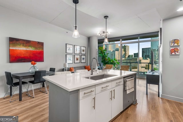 kitchen with sink, decorative light fixtures, white cabinets, an island with sink, and a wall of windows