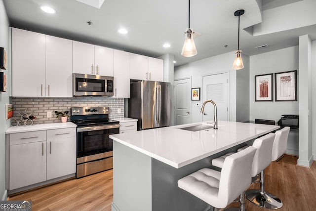 kitchen with stainless steel appliances, white cabinetry, tasteful backsplash, hanging light fixtures, and a kitchen island with sink