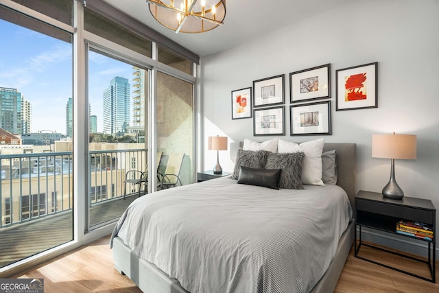 bedroom with a wall of windows, hardwood / wood-style floors, access to outside, and a notable chandelier